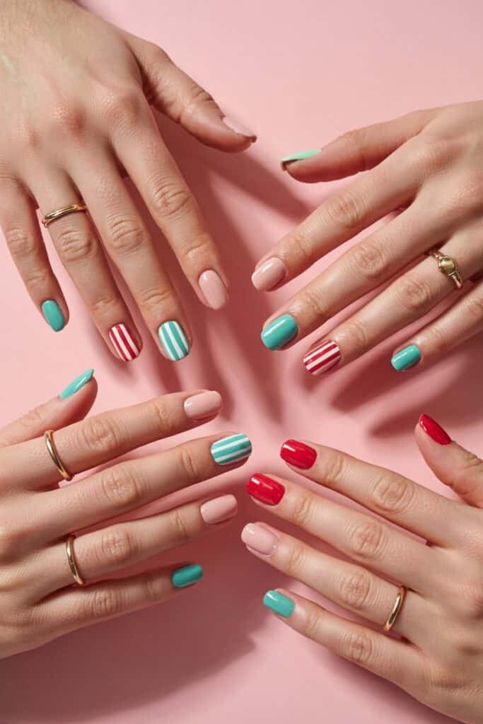 The image shows bright summe nails with colorful manicures on a pink background. Nails feature pastel pink, turquoise, red, and white in solid colors and striped designs, paired with minimal gold rings for a stylish, summery look.