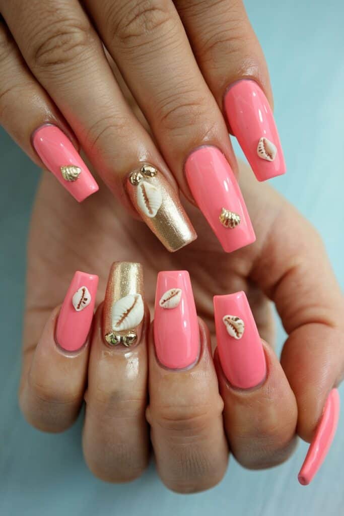 Long coral acrylic nails with gold accents and mini shell charms for a beach-inspired summer look.