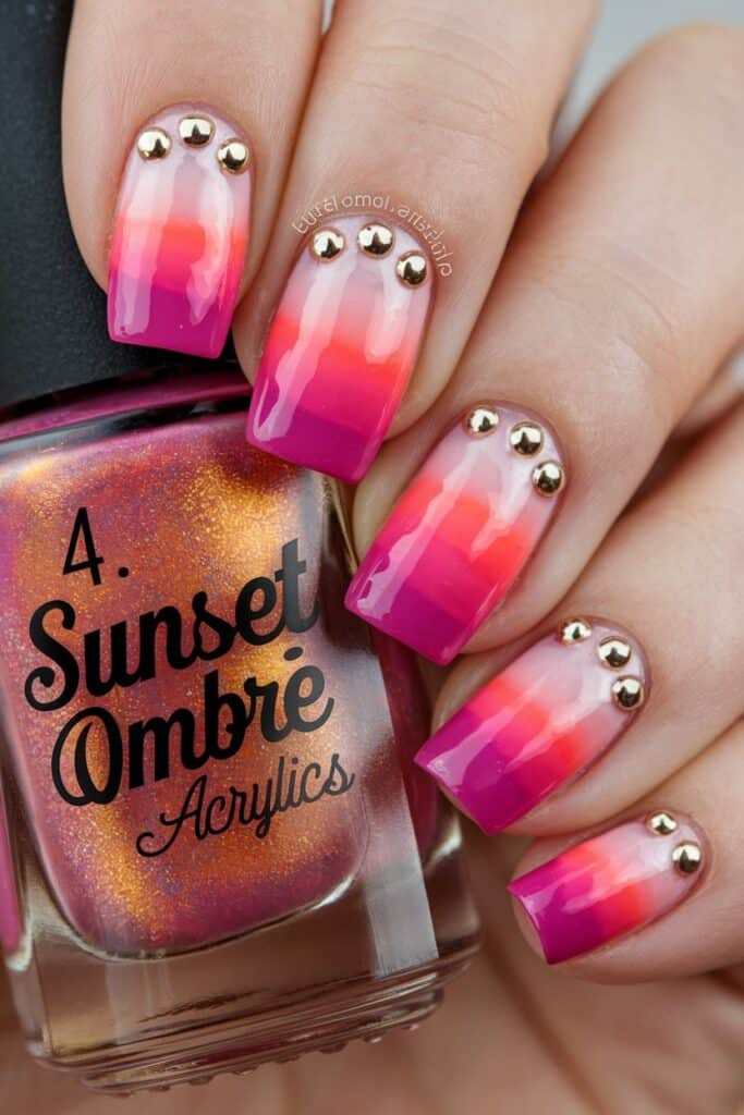 Sunset ombré acrylic nails in pink, coral, and purple tones with gold studs for a radiant summer glow.