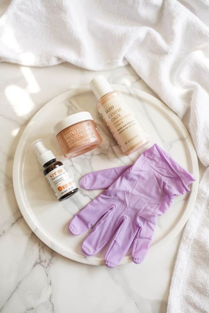 Hand care products including SPF serum, moisturizer, and purple treatment gloves on a marble surface.