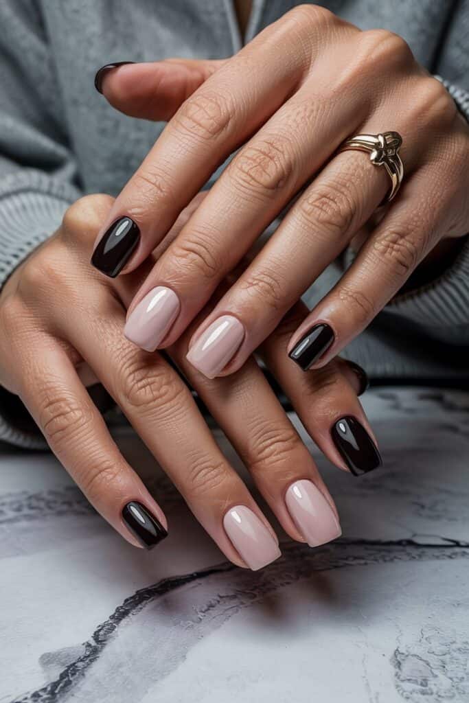 Square nails painted in alternating soft blush pink and dark glossy black. Nails are neatly shaped and the hands are gently resting on a marble-textured surface.