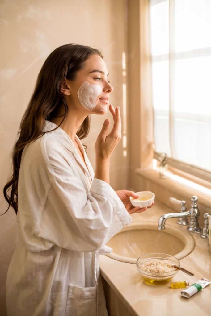 a woman in a bathrobe applying cream on her face