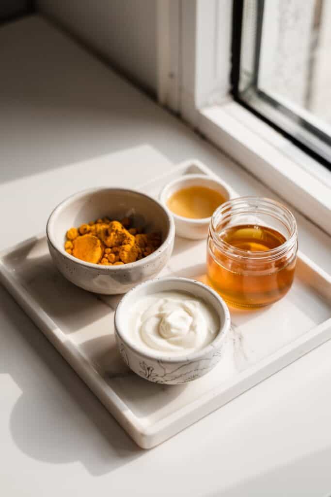 Fresh turmeric powder, honey, and yogurt ingredients arranged neatly for a homemade face mask.
