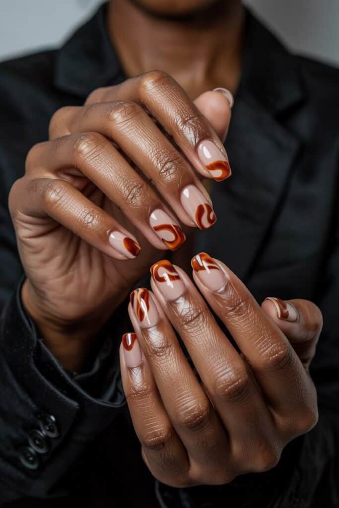 5. **Burnt Orange and Nude Swirls**: Short nails featuring artistic swirls of burnt orange polish over a neutral nude base.

