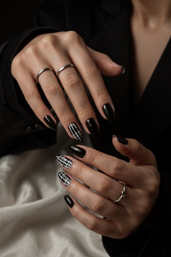 Short black nails with a detailed skeleton hand design on one accent nail for Halloween edge.
