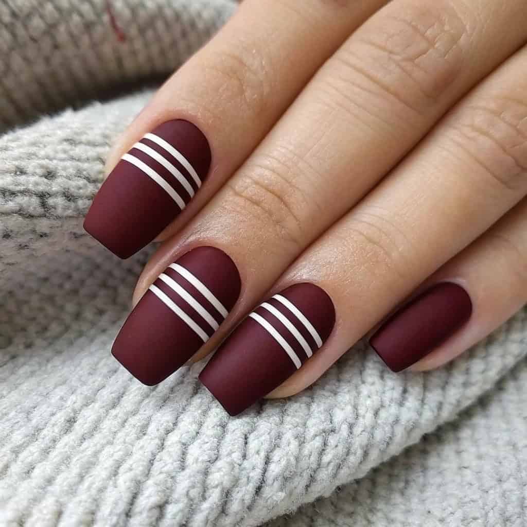 Dark cherry red nails with a matte finish and white stripes