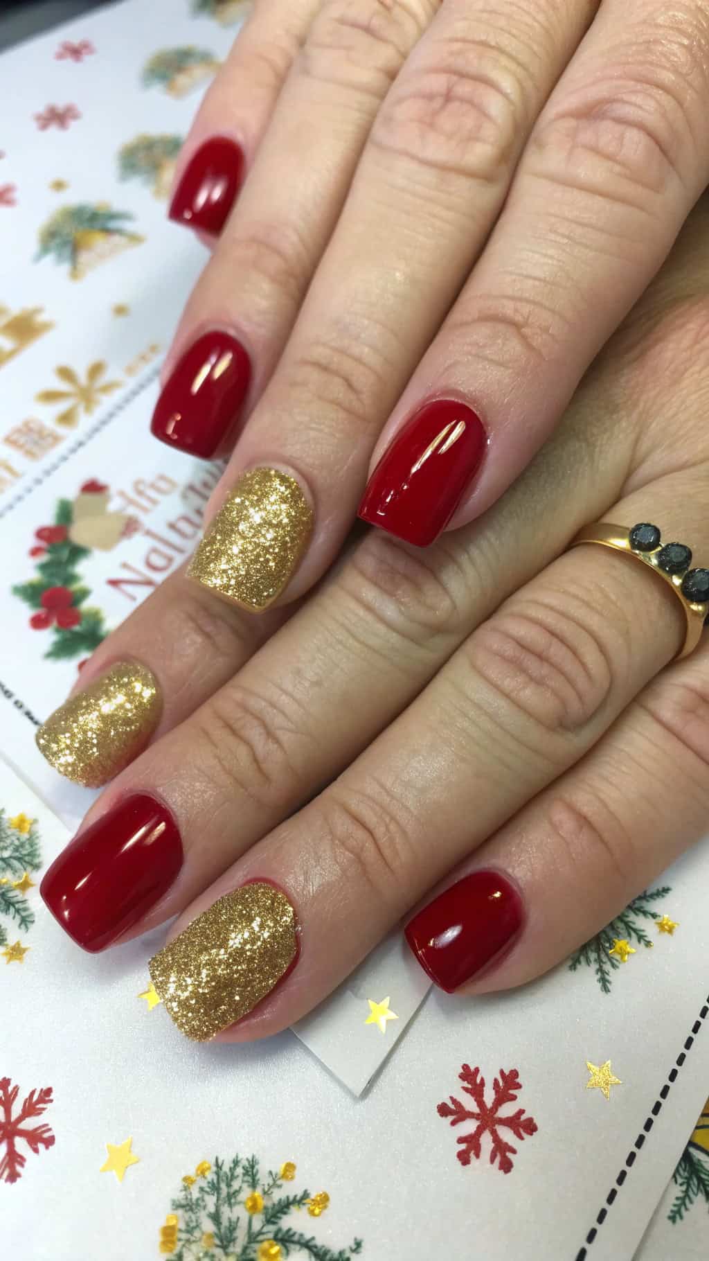 Close-up of festive red nails with gold glitter tips, set against a holiday-themed background.