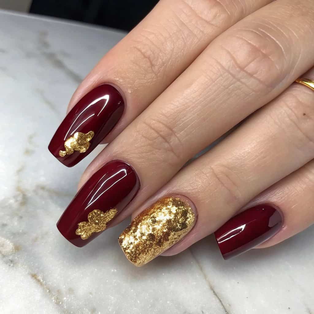 Dark cherry red nails with gold foil accents on a marble background