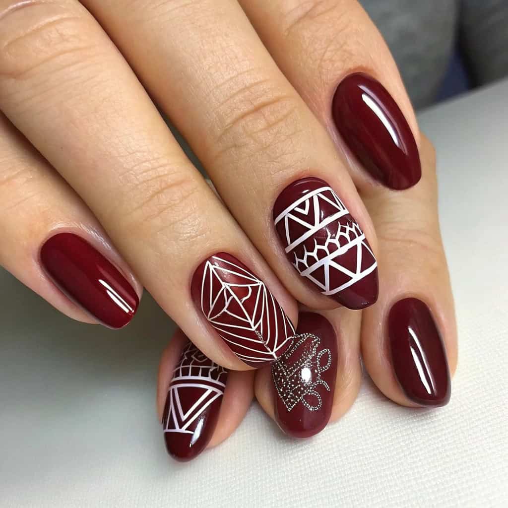 A stylish dark cherry red manicure featuring negative space and white floral designs.