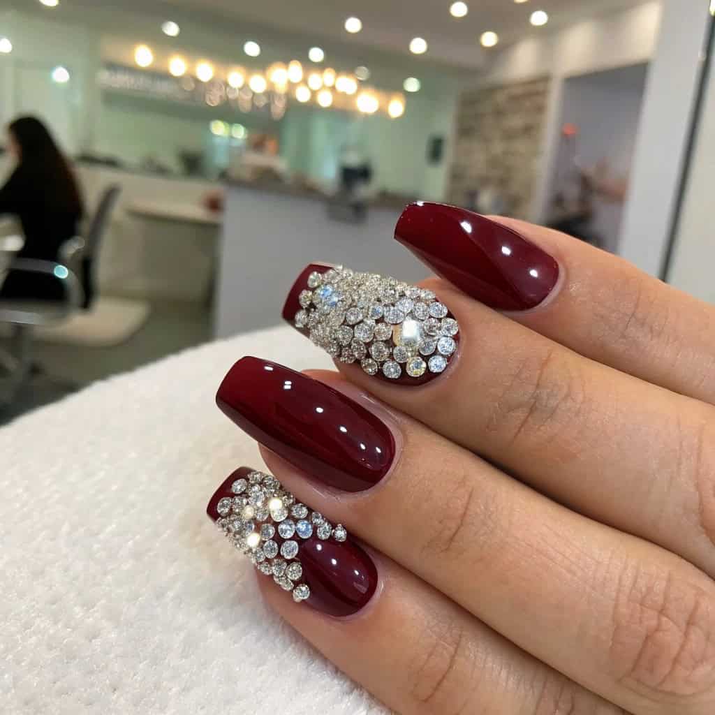 Dark cherry red nails with rhinestones, showcasing a mix of solid and embellished designs.