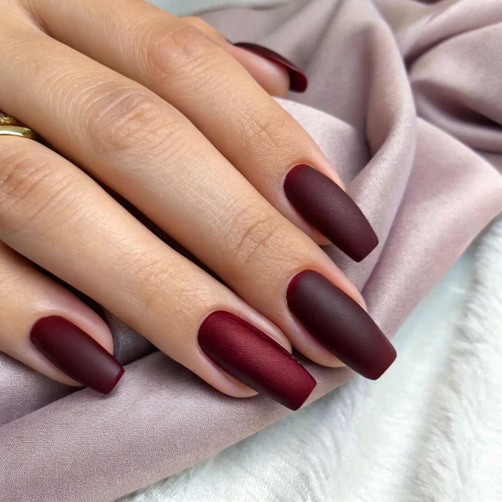 Matte dark cherry red nails with glossy tips on a soft pink fabric