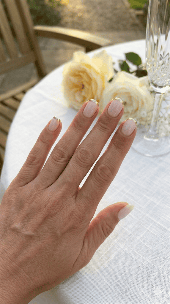 Elegant champagne gold micro-French tip manicure on a medium-tan mature hand, squoval shape, high-contrast white tablecloth background.