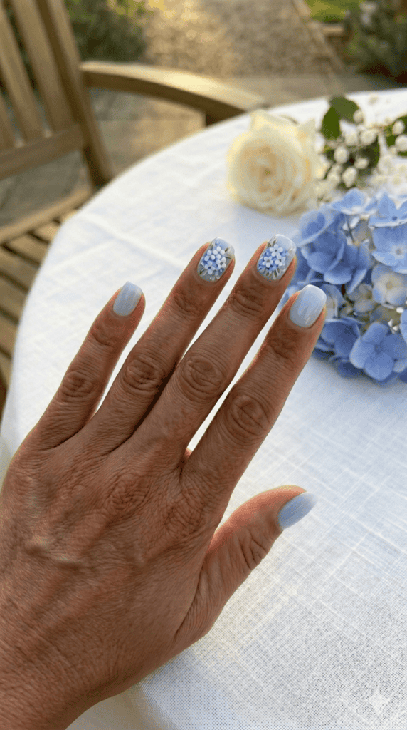 Intricate blue hydrangea floral nail art on a light-medium skin tone, sophisticated wedding guest manicure, luxury indoor reception setting.
