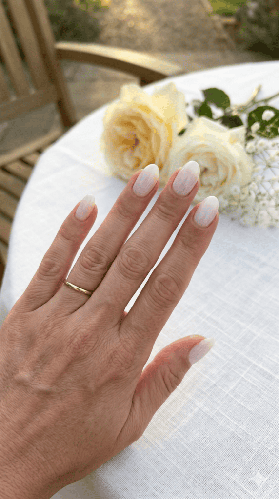 Summer wedding guest nails that are sophisticated milky white "glass" nails on medium-tan mature hands, high-gloss finish, high-contrast flat lay on white textured linen.
