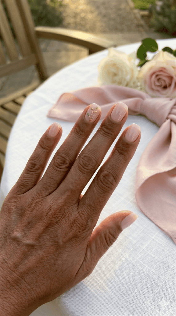 Sheer rosewater pink nails on a deep rich skin tone featuring a delicate gold and sage botanical accent, elegant "Old Money" wedding aesthetic.