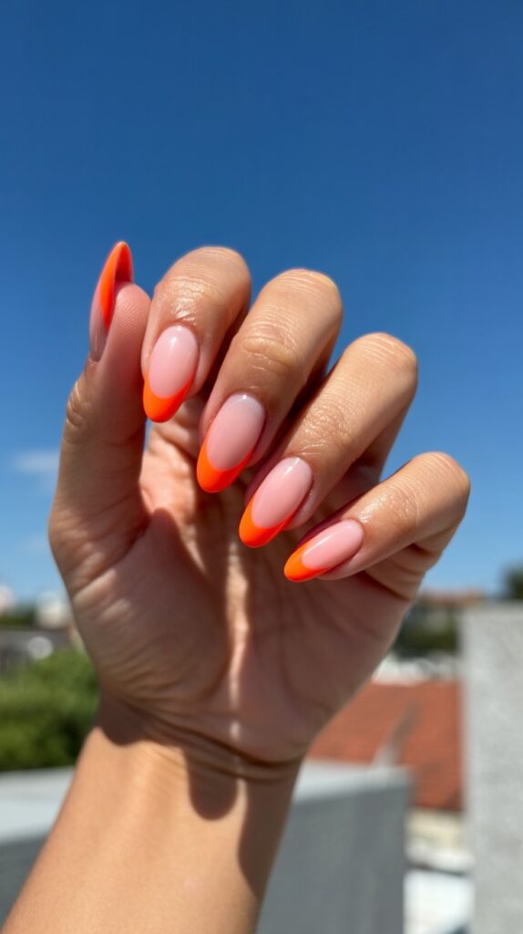 Close-up of almond-shaped nails with bold neon orange micro French tips held up against a vivid blue summer sky, sheer nude base, bright and vibrant outdoor light

