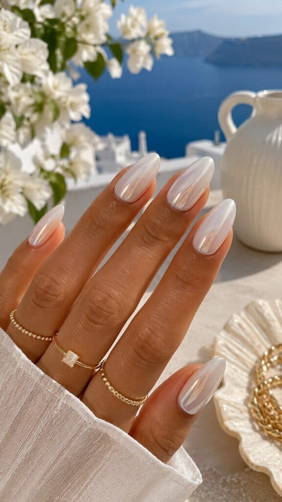 Pearl white glazed nails with iridescent shimmer on almond shape, Santorini-style background